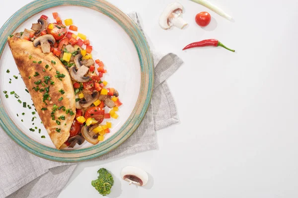 Вид сверху на тарелку с вкусным домашним завернутым омлетом с овощами на белом столе со свежими ингредиентами — стоковое фото