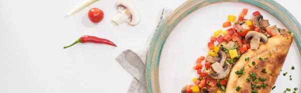 Верхний вид тарелки с вкусным обернутым омлетом с овощами на белом столе со свежими ингредиентами — стоковое фото