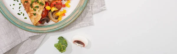 Вид сверху на вкусный завернутый омлет с овощами на тарелке с ингредиентами — стоковое фото