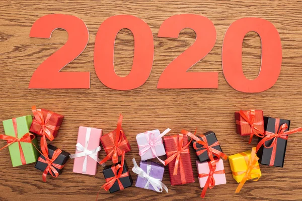 Vista superior de los números de papel 2020 cerca de pequeñas cajas de regalo decorativas sobre fondo de madera - foto de stock