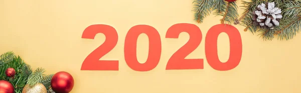 Top view of paper 2020 numbers near christmas tree branch with baubles on yellow background, panoramic shot — Stock Photo