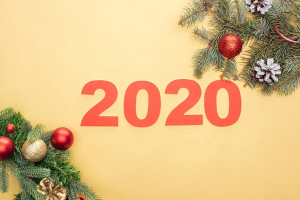 Draufsicht auf Papier 2020 Zahlen in der Nähe von Weihnachtsbaumzweigen mit Kugeln und Zapfen auf gelbem Hintergrund — Stockfoto