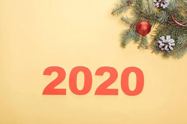 Top view of paper 2020 numbers near christmas tree branch with baubles and cones on yellow background — Stock Photo