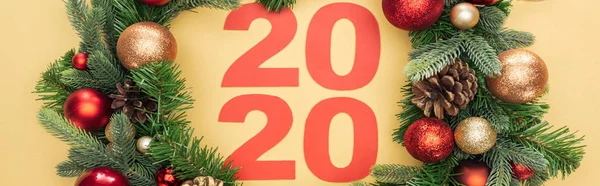 Top view of paper 2020 numbers in christmas wreath with baubles on yellow background, panoramic shot — Stock Photo