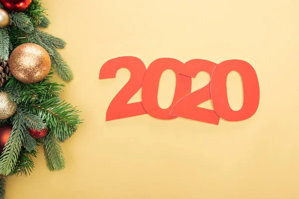 Vista superior de los números de papel 2020 cerca de la rama del árbol de Navidad con adornos sobre fondo amarillo - foto de stock