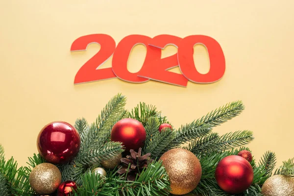 Paper 2020 numbers near christmas tree branch with baubles on yellow background — Stock Photo