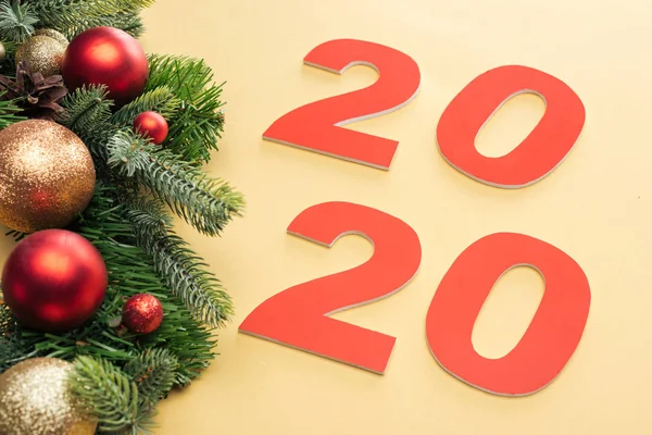 Papier 2020 Zahlen in der Nähe von Weihnachtsbaum Zweig mit Kugeln auf gelbem Hintergrund — Stockfoto