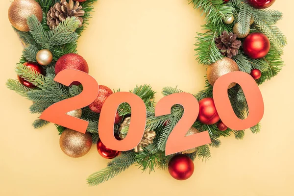 Top view of paper 2020 numbers on christmas wreath with baubles on yellow background — Stock Photo