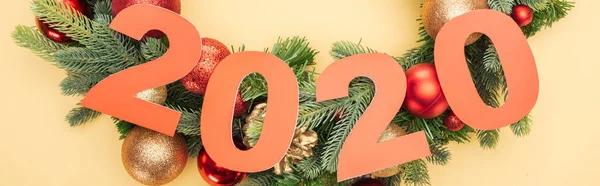 Vista superior de los números de papel 2020 cerca de la rama del árbol de Navidad con adornos sobre fondo amarillo - foto de stock