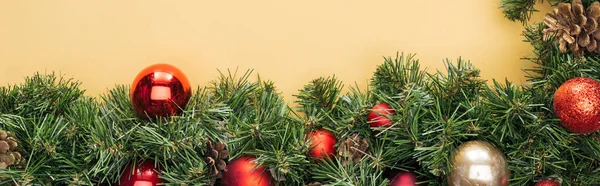 Top view of christmas tree branch with red and golden baubles on yellow background, panoramic shot — Stock Photo