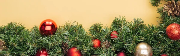 Vista superior do ramo de árvore de natal com bugigangas vermelhas e douradas no fundo amarelo, tiro panorâmico — Fotografia de Stock