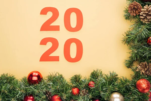 Vista superior de los números de papel 2020 cerca de la rama del árbol de Navidad con adornos sobre fondo amarillo - foto de stock