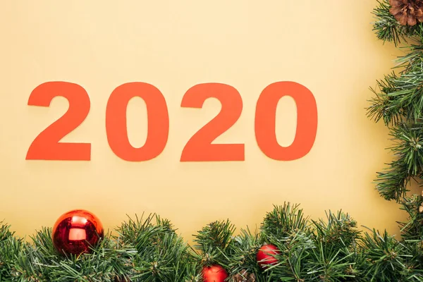 Vista superior de los números de papel 2020 cerca de la rama del árbol de Navidad con adornos sobre fondo amarillo — Stock Photo