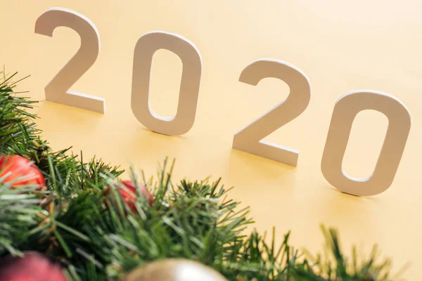 Paper 2020 numbers near Christmas tree branch with baubles on yellow background — Stock Photo