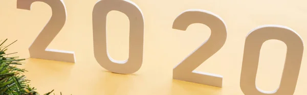 Paper 2020 numbers near Christmas tree branch on yellow background, panoramic shot — Stock Photo