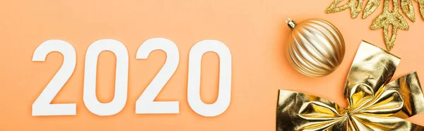 Top view of white 2020 numbers near golden christmas decoration on orange background, panoramic shot — Stock Photo