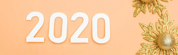 Top view of white 2020 numbers near golden christmas decoration on orange background, panoramic shot — Stock Photo