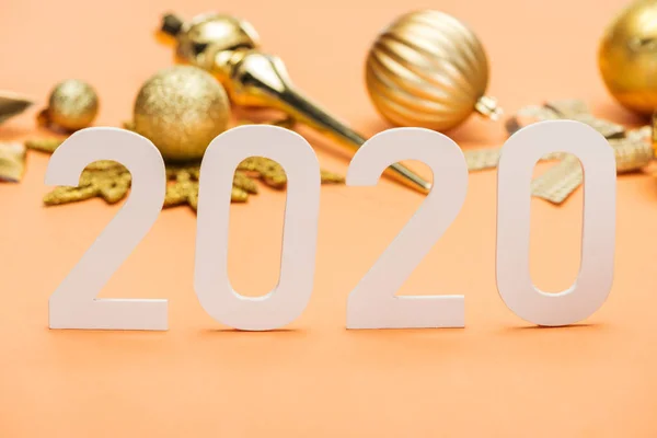Enfoque selectivo de los números blancos 2020 delante de la decoración de Navidad dorada sobre fondo naranja - foto de stock