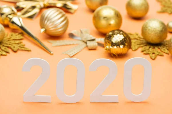 White 2020 numbers near golden christmas decoration on orange background — Stock Photo