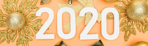 Top view of white 2020 numbers on golden christmas decoration on orange background, panoramic shot — Stock Photo