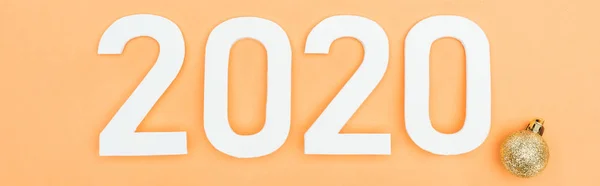 Top view of white 2020 numbers near golden bauble on orange background, panoramic shot — Stock Photo