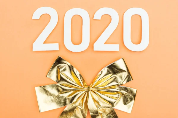 Top view of white 2020 numbers near golden bow on orange background — Stock Photo