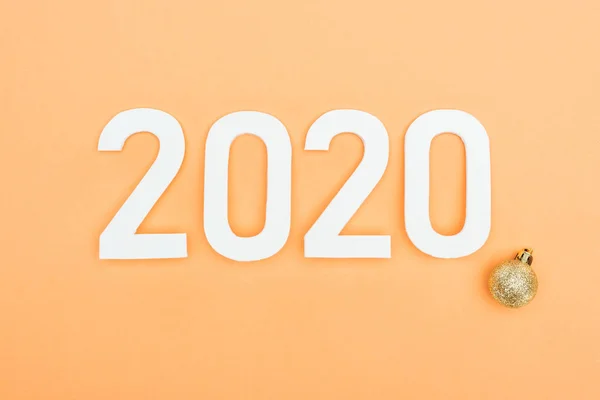 Top view of white 2020 numbers near golden christmas bauble on orange background — Stock Photo