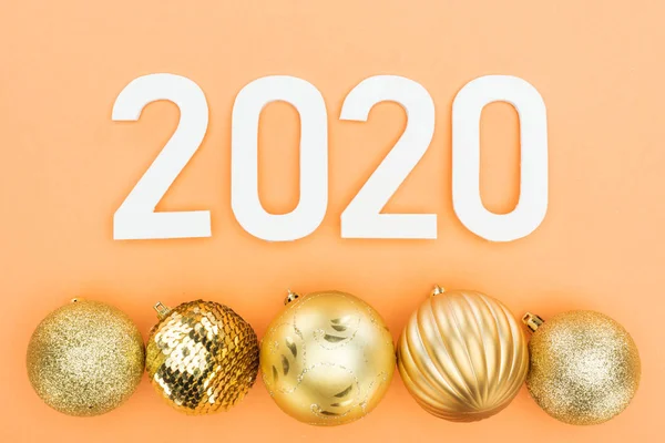 Top view of white 2020 numbers near golden christmas baubles on orange background — Stock Photo