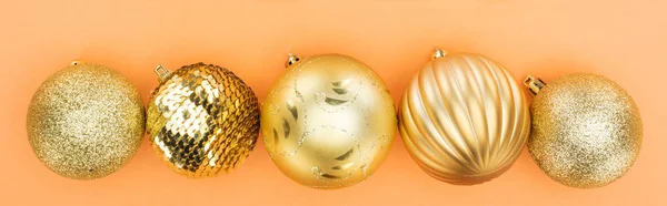 Top view of golden christmas baubles in row on orange background, panoramic shot — Stock Photo