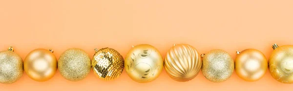 Top view of golden christmas baubles in row on orange background, panoramic shot — Stock Photo