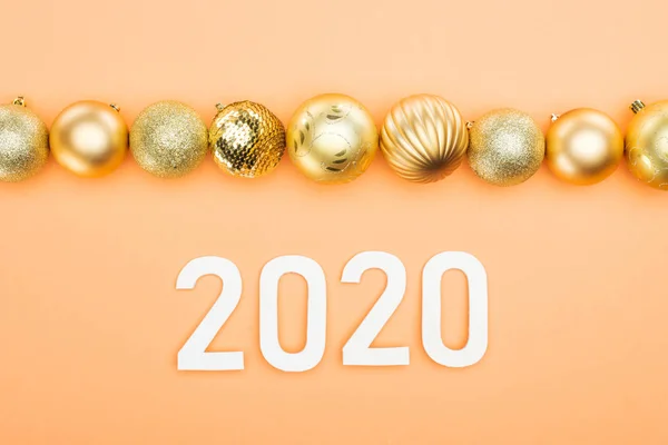 Top view of white 2020 numbers near golden christmas baubles on orange background — Stock Photo