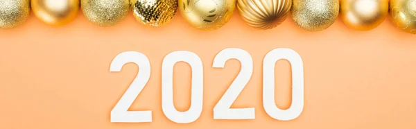 Top view of white 2020 numbers near golden baubles on orange background, panoramic shot — Stock Photo