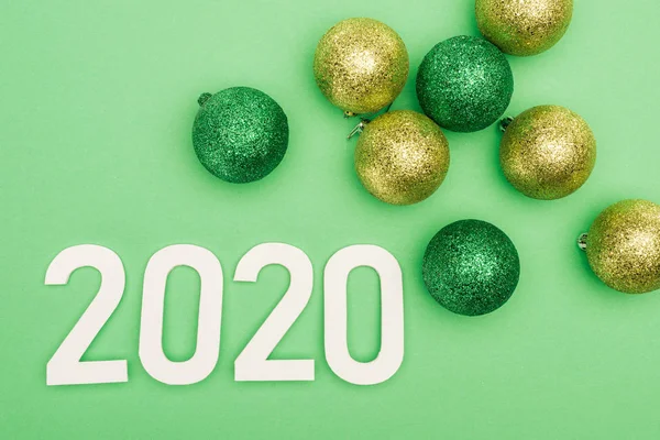 Top view of white 2020 numbers near christmas baubles on green background — Stock Photo