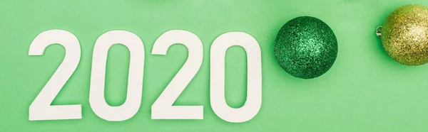 Top view of white 2020 numbers near christmas baubles on green background, panoramic shot — Stock Photo