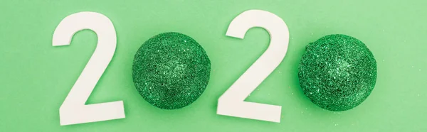 Top view of white 2020 numbers with christmas baubles on green background, panoramic shot — Stock Photo