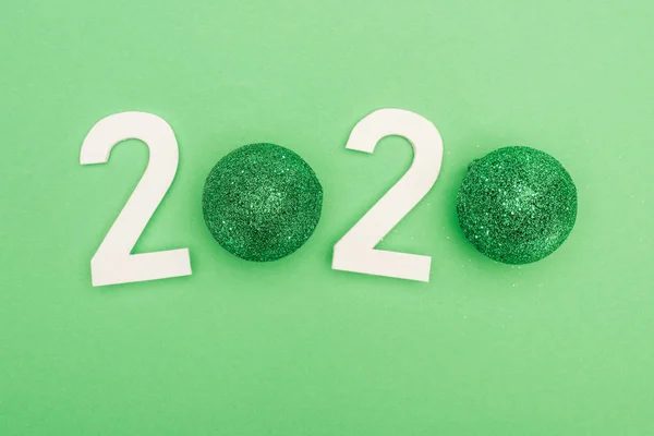 Top view of white 2020 numbers with christmas baubles on green background — Stock Photo