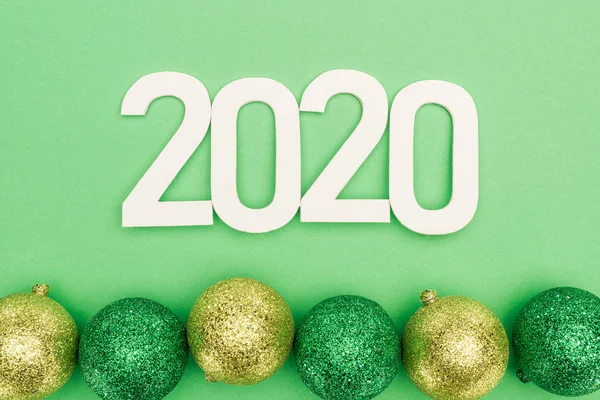 Top view of white 2020 numbers near christmas baubles on green background — Stock Photo