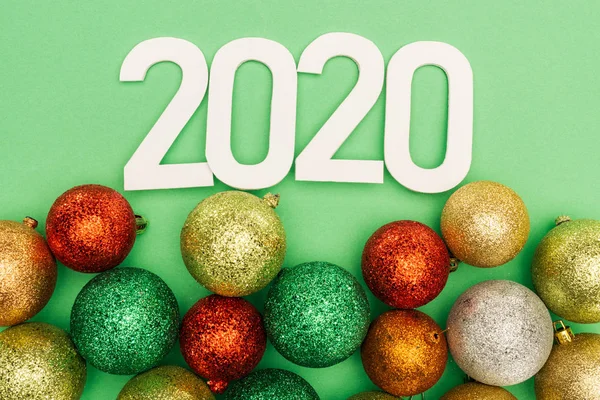 Top view of white 2020 numbers near multicolored Christmas baubles on green background — Stock Photo