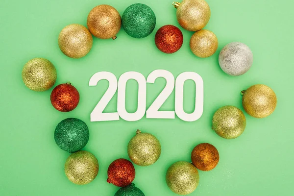 Top view of white 2020 numbers near multicolored Christmas baubles on green background — Stock Photo