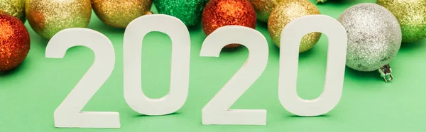 Números blancos 2020 cerca de bolas de Navidad multicolores sobre fondo verde, tiro panorámico - foto de stock