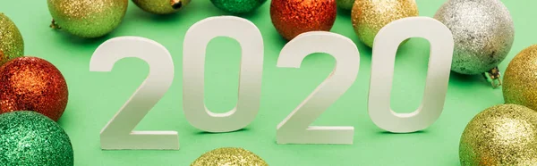 White 2020 numbers near multicolored Christmas baubles on green background, panoramic shot — Stock Photo