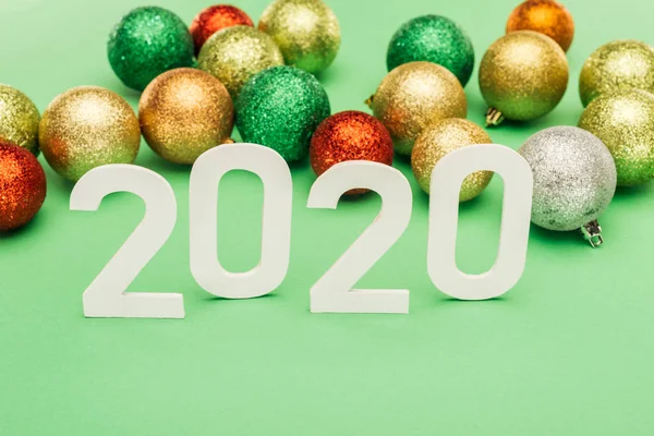 White 2020 numbers near multicolored Christmas baubles on green background — Stock Photo