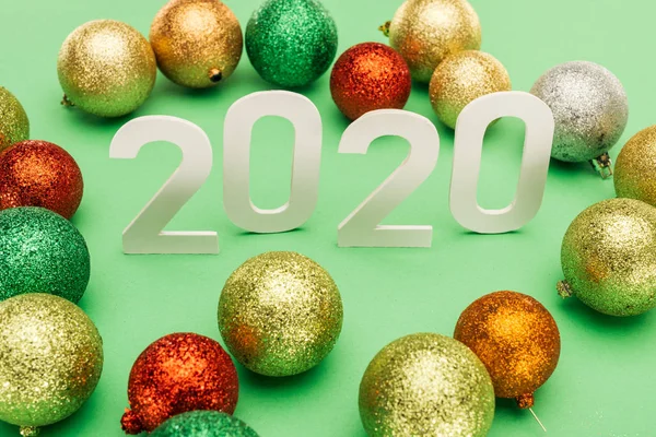 White 2020 numbers near multicolored Christmas baubles on green background — Stock Photo