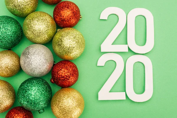 Top view of white 2020 numbers near multicolored Christmas baubles on green background — Stock Photo