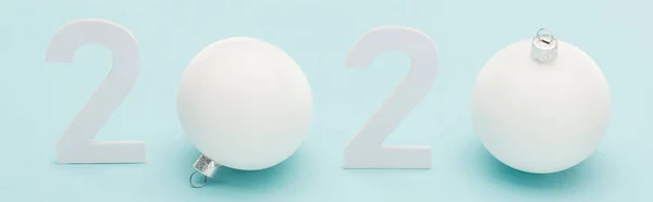 White 2020 numbers near Christmas baubles on light blue background, panoramic shot — Stock Photo