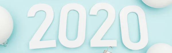 Top view of white 2020 numbers near Christmas baubles on light blue background, panoramic shot — Stock Photo
