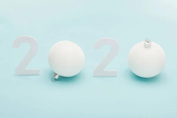 Números blancos 2020 cerca de bolas de Navidad sobre fondo azul claro - foto de stock