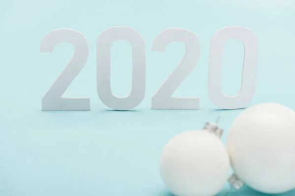Selective focus of white 2020 numbers near Christmas baubles on light blue background — Stock Photo