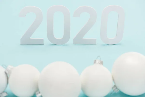 Selective focus of white 2020 numbers near Christmas baubles on light blue background — Stock Photo