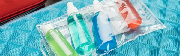 Colpo panoramico di bottiglie luminose con liquidi e borsa cosmetica sulla borsa da viaggio — Foto stock